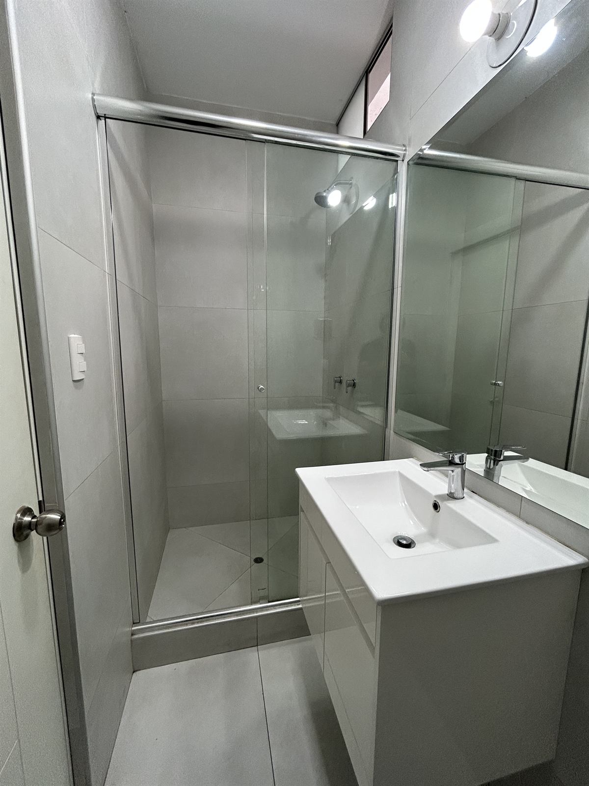Baño con ducha de mampara de vidrio y lavabo colgante blanco