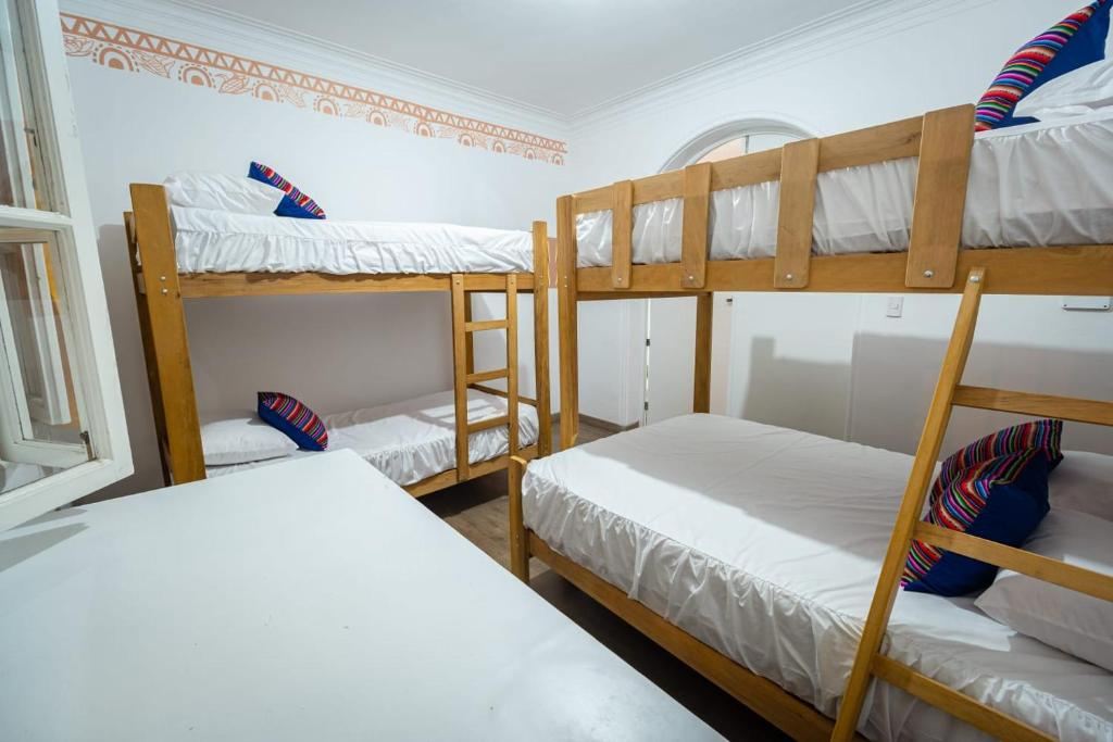 Dormitorio compartido de Casa Águila y Cóndor con literas de madera, ropa de cama blanca y cojines andinos