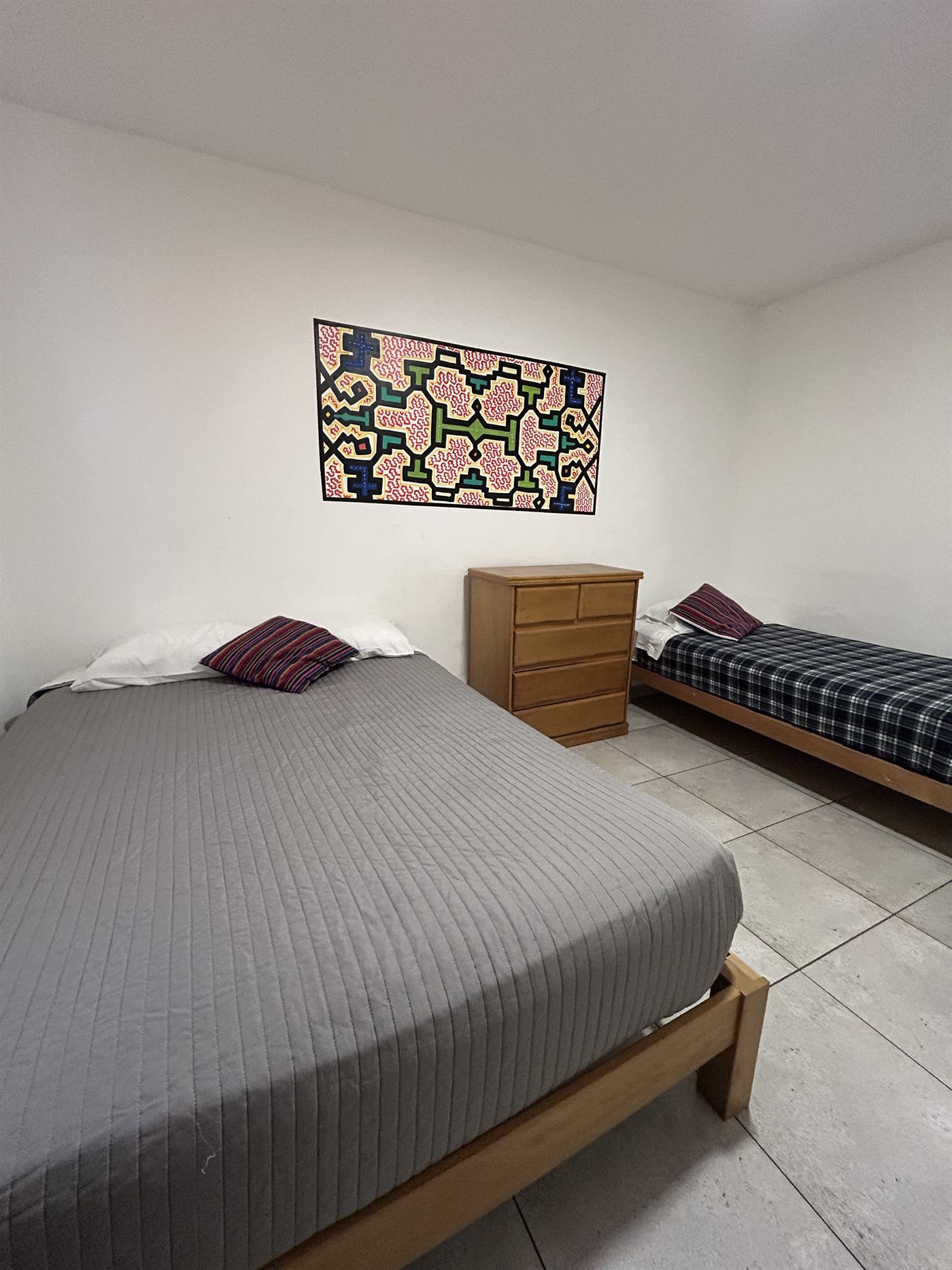 Habitación privada con cama doble, cama individual y arte shipibo enmarcado en la pared