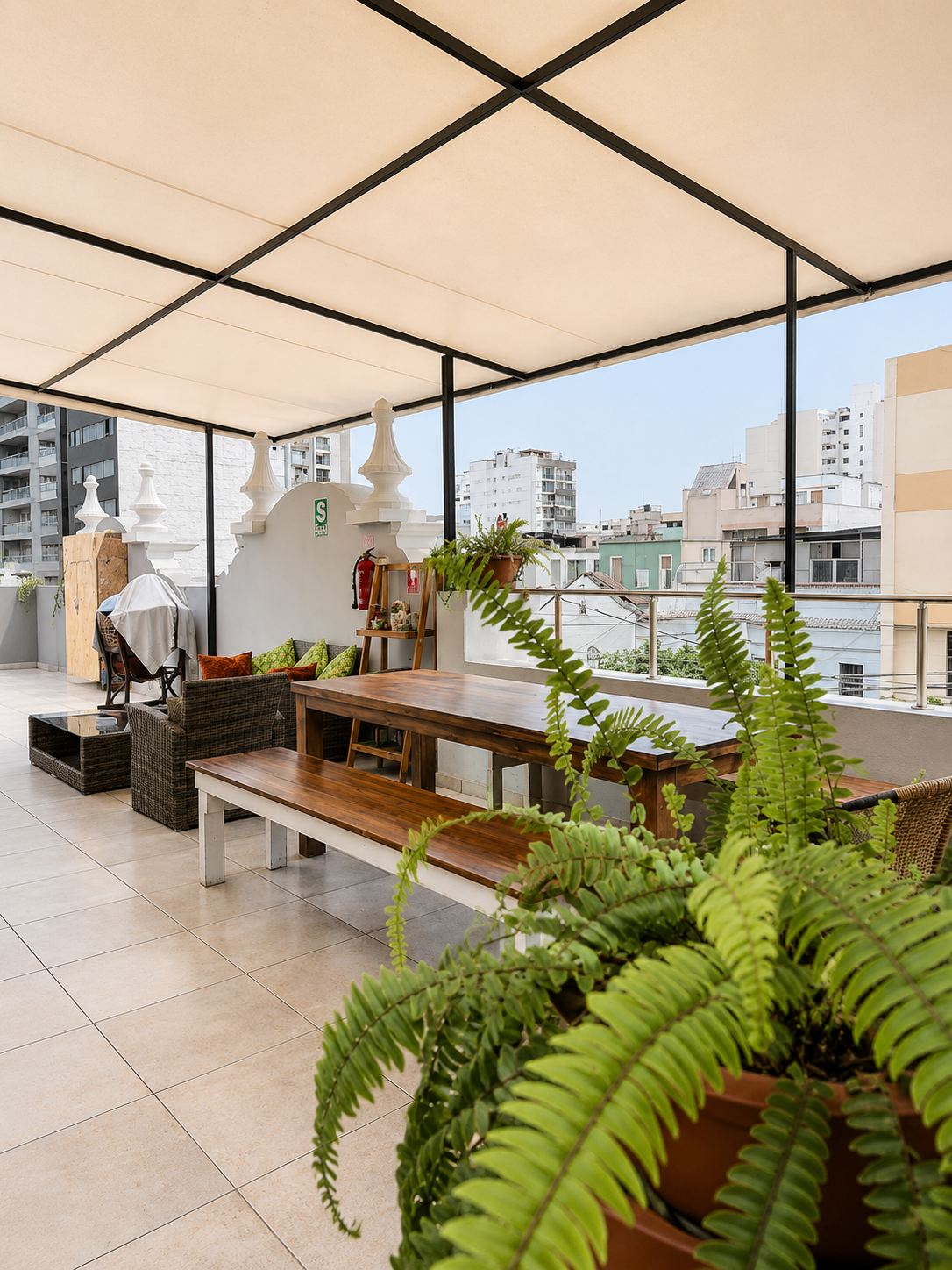 Terraza techada de Casa Águila y Cóndor con mesa larga de madera, helechos y vista a los techos de Miraflores